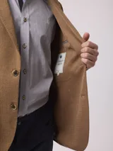 Saco de lino color tostado, de corte clásico, con solapa de muesca, cierre de dos botones, bolsillo en el pecho y bolsillos laterales con solapa.