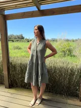 Vestido verde militar de lino, corte a la rodilla, sin mangas, con cuello mao y botones de nácar. Presenta varios cortes en su largo, aportando movimiento y un toque moderno a este diseño fresco y elegante.