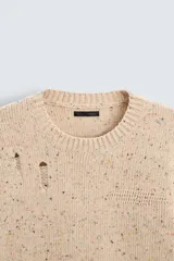 Sweater color beige con motas de colores, de tejido de punto grueso con cuello redondo y mangas largas. Presenta roturas y agujeros en el frente y las mangas.