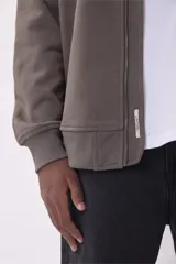 Campera bomber color marrón topo, con cierre frontal y bolsillos laterales con cierre. Tiene un bolsillo con cierre y etiqueta en la manga izquierda.