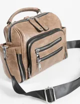 Mochila bandolera color marrón de cuero sintético con múltiples bolsillos con cierre plateado y correa de tela negra ajustable.