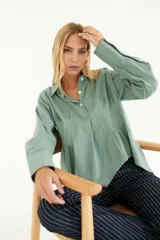 Camisa color crema de algodón, con cuello polo, mangas largas con puños abotonados y corte asimétrico.