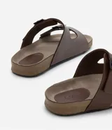 Sandalias slide marrones de cuero sintético con dos tiras ajustables con hebillas metálicas negras y plantilla anatómica.