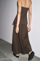 Vestido midi marrón confeccionado en hilatura 24% de lino. Escote recto y hombros descubiertos. Cierre en espalda con cremallera oculta en costura.