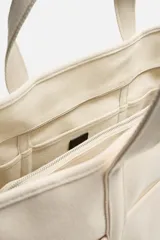 Bolso tipo shopper color crema, fabricado en tejido de algodón. Tiene doble asa de mano, compartimento principal con cierre de cremallera, seis bolsillos planos interiores, funda interior para dispositivos electrónicos de hasta 13 pulgadas con cierre de cremallera, bolsillo plano frontal y bolsillos planos laterales.