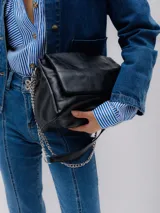 Bolso negro acolchado con efecto cuero, solapa y cadena plateada. Tiene cierre magnético y bolsillo interior con cierre.