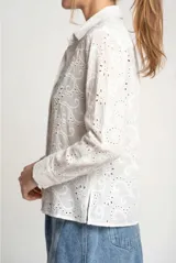 Blusa blanca de manga larga con cuello camisero, confeccionada en algodón con bordados calados (broderie) de diseño floral y arabesco.