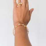 Pulsera dorada de acero quirúrgico bañada en rodio, con tres vueltas y perlas blancas.