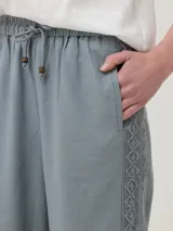 Pantalón gris de lino y viscosa con ajuste elástico y cordón en la cintura. Presenta broderie tono a tono en los laterales y en la parte inferior.