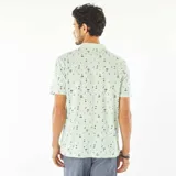 Remera polo verde claro con estampado de palmeras y tablas de surf en negro.