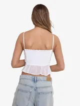 Blusa blanca sin mangas con tirantes finos, escote en V y volados con detalles de encaje.