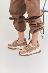 Zapatillas deportivas con diseño moderno en tonos blancos y dorados, con cierre de velcro para mayor comodidad.
