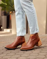 Botas de cuero color marrón, hechas a mano, con punta en pico y taco de madera cuadrado. Cierre lateral con cremallera.