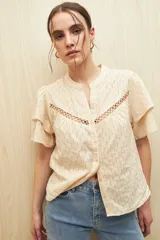 Camisa blanca de algodón liviano con diseño calado, cuello mao, mangas cortas abullonadas y detalle de pasamanería en el frente.