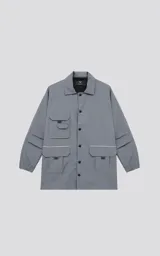 Campera gris de tejido liviano, con cuello camisero, cierre frontal de broches y puños elásticos. Presenta múltiples bolsillos cargo en el frente con ribetes reflectantes blancos.