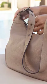 Cartera negra ovalada de simil cuero con cierre y correa ajustable con ojales. Cuenta con bolsillos internos y un bolsillo trasero.