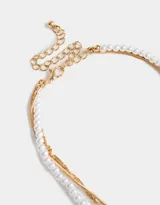Collar dorado de tres capas: una de perlas, una de cadena de eslabones y una de cadena retorcida con dije de corazón con rosa grabada y moño.