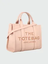 Bolso tote de cuero negro Marc Jacobs, tamaño mediano, con doble asa corta y correa larga extraíble. Estampado frontal con el texto "THE TOTE BAG" y el nombre de la marca.