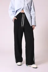 Pantalón negro de corte ancho con cintura elastizada y cordón ajustable. Presenta una franja blanca vertical a lo largo de la pierna.