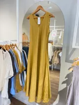 Vestido largo sin mangas, color mostaza, con escote en V y bordes deshilachados en sisas y ruedo.