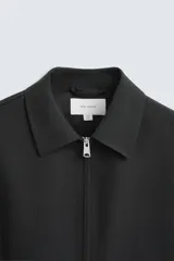 Sobrecamisa negra de lana con cuello solapa, manga larga con puños abotonados, bolsillos de vivo en la cadera y cierre frontal con cremallera.