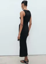 Vestido midi negro, sin mangas, con cuello redondo y tirantes anchos. Presenta un nudo decorativo en la cintura que cae como un lazo.