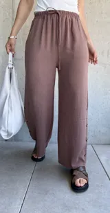 Pantalón marrón de tela texturizada, corte ancho, cintura elastizada con cordón ajustable y botones decorativos en los laterales.