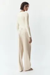 Pantalón de vestir color crema, de tiro alto y pernera ancha, con pinzas delanteras, bolsillos frontales y falsos bolsillos de doble vivo en la espalda.