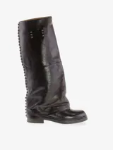 Bota alta de cuero bovino color negro con diseño de caña ancha y efecto doblado. Presenta detalles de tachas metálicas a lo largo de la costura posterior y una placa metálica decorativa en la parte superior. Cuenta con tacón bajo y punta redondeada.