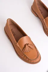 Mocasines de cuero color marrón claro con detalle de borlas en el empeine y costuras decorativas.