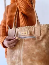 Bolso tipo tote de cuero color camel, con costuras a la vista y tiras de ajuste laterales.