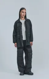 Campera negra oversize con broches en el delantero, forrada con red, múltiples bolsillos con detalles en réflex y puños elásticos en las mangas.