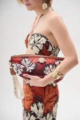 Neceser tipo riñonera de lona estampada con flores en tonos rojo, blanco y negro. Tiene cierre superior con cremallera y correa de tela con logo de la marca.