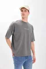 Camiseta manga corta gris oscuro con estampa de un paisaje marino y texto en color blanco. Corte amplio y recto, con proporciones cuadradas.