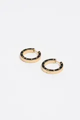 Caravanas de aro doradas con esmalte negro y letras doradas que forman el logo de la marca. Presentan un diseño circular con cierre de gancho para mayor seguridad.