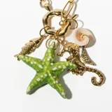 Collar dorado con cadena de eslabones grandes y dijes colgantes con motivos marinos: estrella de mar verde con lunares blancos, pez dorado, caracol blanco y dorado, y caballito de mar dorado.