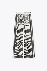 Pantalón de tiro medio con cintura elástica y pierna ancha. Presenta un estampado de líneas onduladas en blanco y negro, y aberturas laterales ajustables con lazadas.