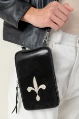 Bolso pequeño tipo 'pocket bag' de cuero vacuno negro, con bordado de flor de lis en color beige claro en el bolsillo frontal. Posee cierre principal, bolsillo trasero y correa desmontable.