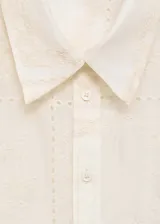 Camisa blanca con bordado de flores y detalles calados, de corte recto y manga larga con puños abotonados. Confeccionada en lyocell y poliéster.