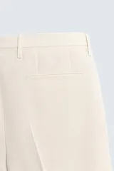 Pantalón de vestir color beige claro, corte regular fit, con pliegues frontales, bolsillos laterales y bolsillos traseros de vivo.