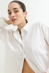 Camisa blanca de corte amplio, con cuello clásico, cierre frontal con botones y mangas largas con puños abotonados.
