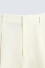 Pantalón color crema de lino, corte relaxed fit, con pliegues frontales, bolsillos laterales y traseros de vivo.