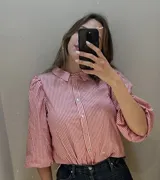 Camisa a rayas verticales rojas y blancas, con cuello bebé, mangas 3/4 abullonadas y botones nacarados.