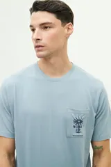 Remera celeste de manga corta con bolsillo en el pecho y estampado con palmera y texto.