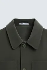 Sobrecamisa negra de corte amplio, con cuello solapa, manga larga con puños abotonados, bolsillos de parche en el pecho, bolsillos laterales y cierre frontal con botones.