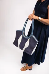 Bolso tipo tote de cuero y gamuza azul con diseño de ondas blancas. Tiene doble asa de cuero azul y base de cuero graneado. El exterior es de gamuza y tela 100% algodón.