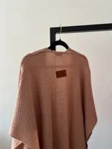 Ruana rosa pastel tejida en acrílico con flecos.