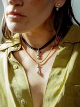 Collar con doble cadena, una tipo choker de cuero negro y otra más larga de cuero color beige, ambas con dije colgante de plata con forma de piedras irregulares.