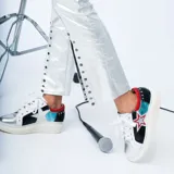 Zapatillas deportivas bajas de cuero con base blanca, puntera plateada, cuerpo negro con estrella blanca y detalles en rojo y turquesa.