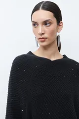Capa tejida color negro, con cuello redondo, diseño de punto y detalles de lentejuelas. Presenta flecos en el dobladillo.